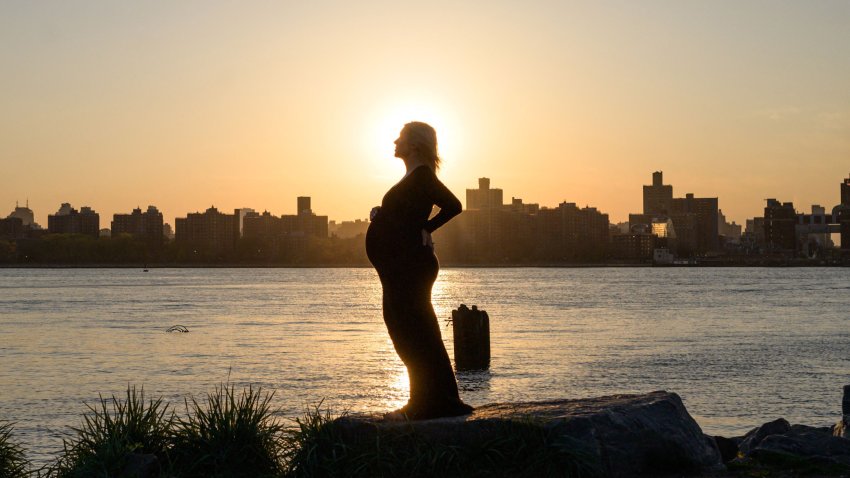 A pregnant woman poses for photos before the Manhattan city skyline at sunset in a park in Williamsburg, New York on April 20, 2021. (Photo by Ed JONES / AFP)