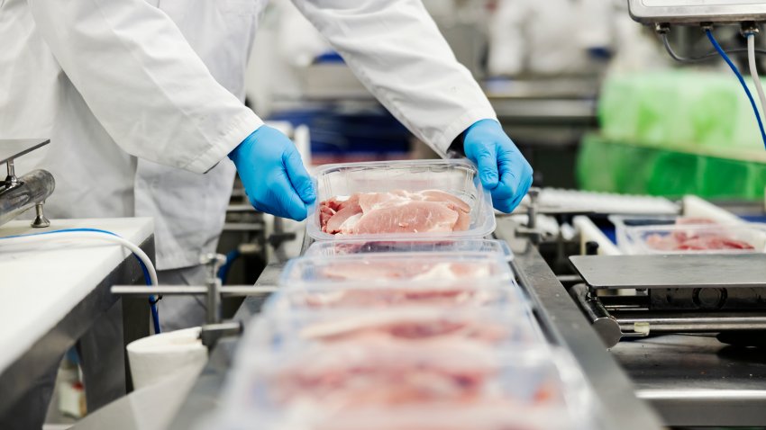 Foto de archivo. Primer plano de un trabajador de la industria cárnica recogiendo carne envasada en una cinta transportadora.