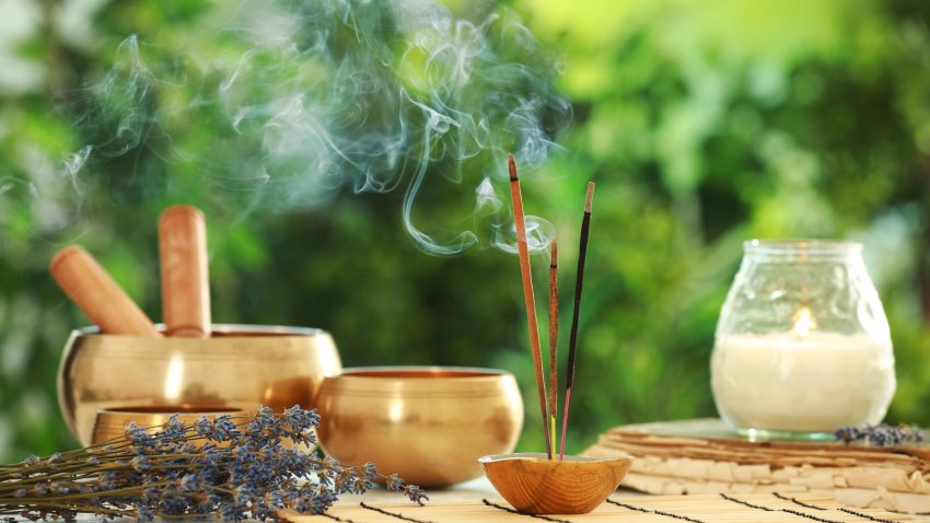 Incense sticks smoldering in holder, Tibetan singing bowls, dried lavender and candle on table outdoors