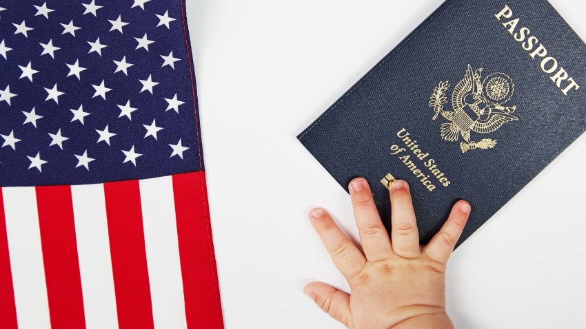 US passport. White background. The baby’s hand reaching for it. USA flag.