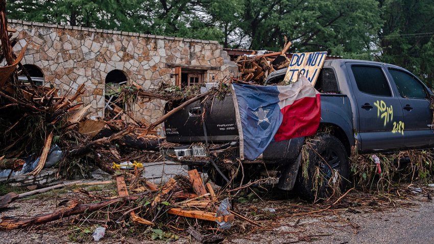 HUNT, TEXAS – JULY 6: A destroyed SUV draped in a Texas State flag sits next to the road after flash flooding swept through the area on July 6, 2025 in Hunt, Texas. Heavy rainfall caused flooding along the Guadalupe River in central Texas with multiple fatalities reported. (Photo by Jim Vondruska/Getty Images)